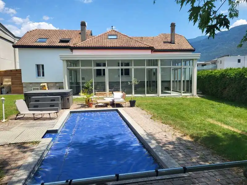 Véranda beige vue du jardin au bord de la piscine